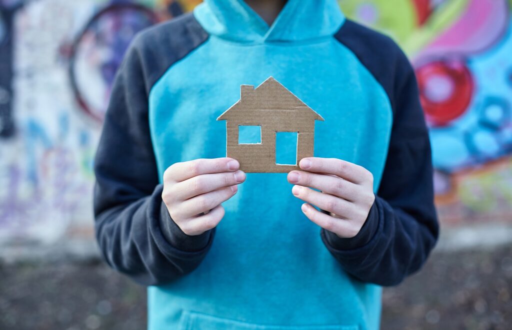 young homeless boy holding a cardboard house