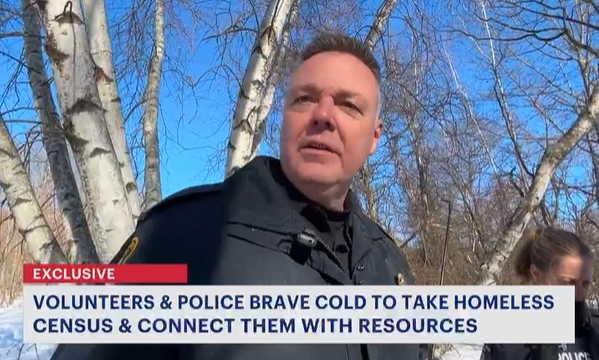 Police officer speaking outdoors in snowy wooded area during homeless outreach effort, with news caption overlay